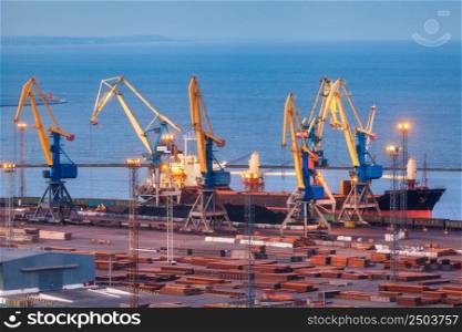 Sea commercial port at night in Mariupol, Ukraine before the war. Industrial. Cargo freight ship with working cranes bridge in sea port at twilight. Cargo port, logistic. Heavy industry