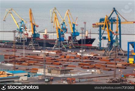 Sea commercial port at night in Mariupol, Ukraine. Industrial view. Cargo freight ship with working cranes bridge in sea port at twilight. Cargo port, logistic