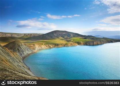 Sea harbor with blue water, green field and blue sky with clouds