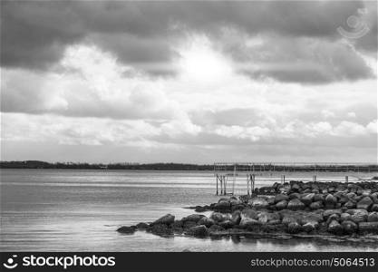 Sea landscape in black and white with an empty bathing pier in cloudy weather