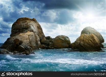 Sea landscape with rock in ocean, dark clouds in sky and bright sun.