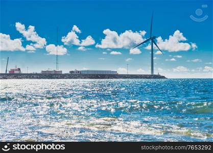 Sea landscape with rocky shore, surf and large windmill at edge of stone breakwater