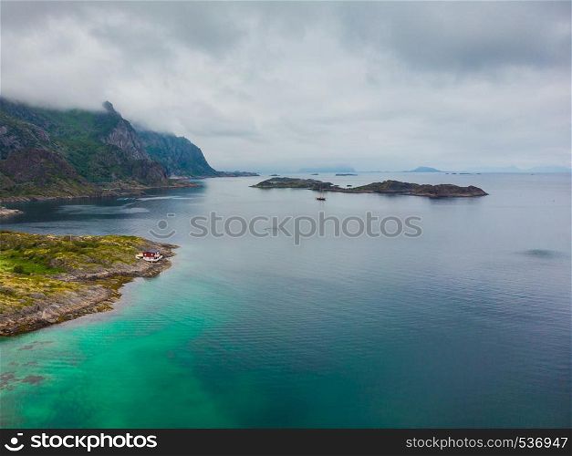 Sea landscape with yacht boat and stone islets among the waters of fjord Vjestfjord, Lofoten islands, Henningsvaer region, Norway. Hazy day, overcast weather.. Aerial view. Lofoten islands landscape, Norway