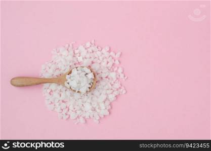 Sea salt in a wooden spoon on pink background for seasoning or preserving food