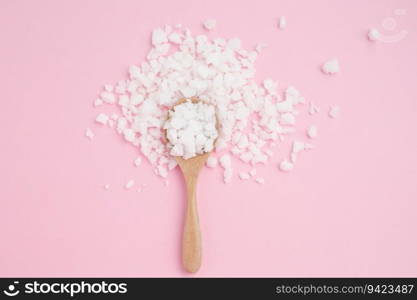 Sea salt in a wooden spoon on pink background for seasoning or preserving food