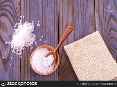 Sea salt on cup, spoon and burlap on a wooden table