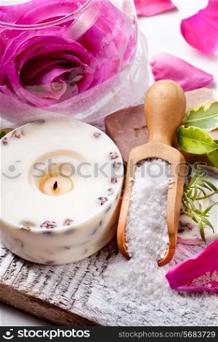 Sea salt, rose, soap and a burning candle on a white table