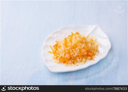 Sea salt with fresh orange zest on white plate on light blue background, selective focus, copy space