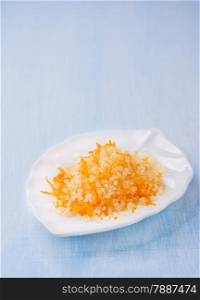 Sea salt with fresh orange zest on white plate on light blue background, selective focus, copy space