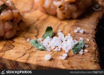 Sea salt with fresh sage on olive wood board, chicken cutlet in the background, selective focus