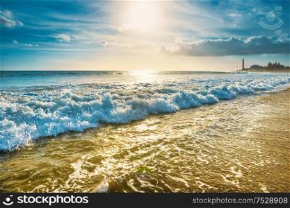 Sea, sand beach with surf waves and lighthouse on background. Maspalomas, Gran Canaria island, Spain