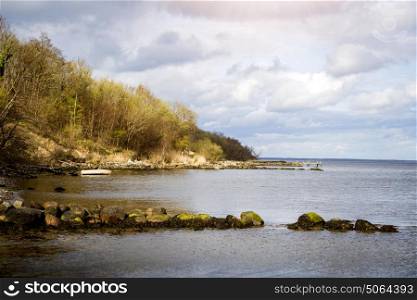 Sea shore with a stranded boat near a forest in Scandinavia with moss covered rocks in the front