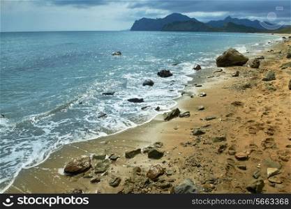 Sea surf, sandy beach with mountains and cloudy sky