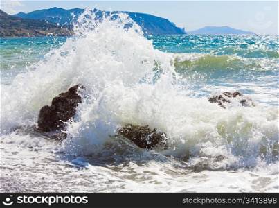 Sea surf wave break on coastline and Meganom cape on horizon right (Crimea, Ukraine)