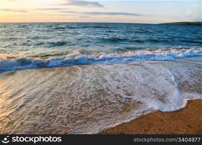 Sea surf wave break on sunset sandy coastline
