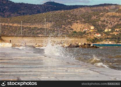 Sea water splashing on the edges of jetty pier reservoir wall in coastline town Greece.. Water splashing on jetty pier