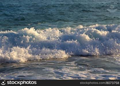Sea waves and white foam in in the rays of the evening sun on the coast