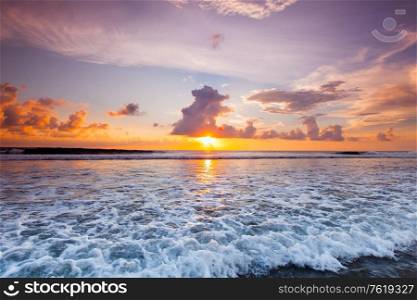 Sea waves at sandy beach at sunset, sun hiding behind a cloud. Sea waves at sunset