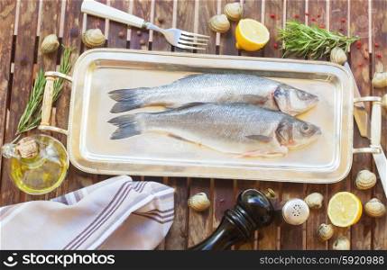 Seabass. Two fresh raw seabass fish on silver tray with frame of spices