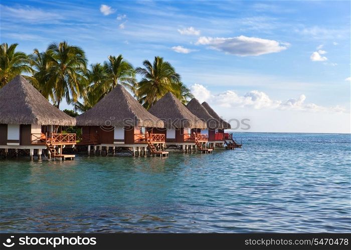 Seacoast with palm trees and small houses on water on a sunset