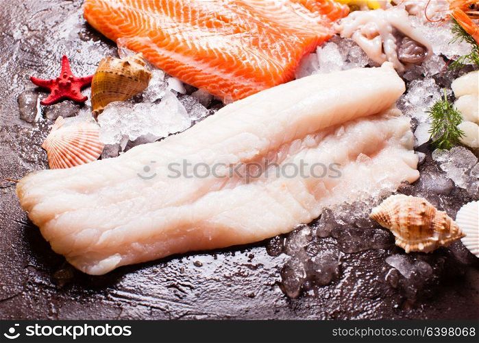 Seafood on the ice, cod fillets close up on the brown slate background. Seafood on the ice