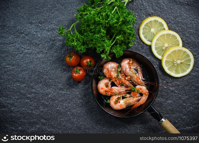 Seafood plate with shrimps prawns cooked on pan with herbs and spices lemon tomato and curly parsley on dark background