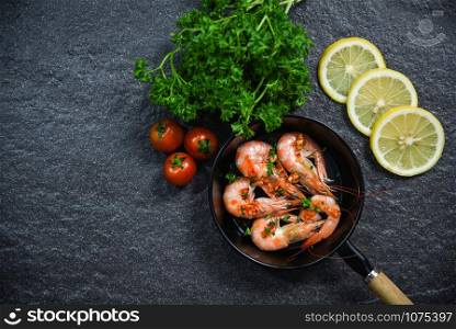 Seafood plate with shrimps prawns cooked on pan with herbs and spices lemon tomato and curly parsley on dark background