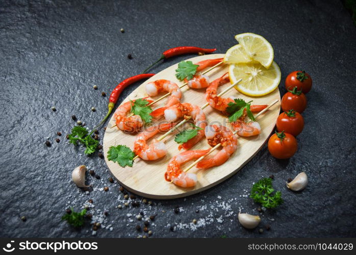 Seafood plate with shrimps prawns skewers seafood cooked with sauce herbs and spices on wooden cutting board background / Close up shellfish shrimp boiled