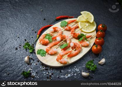 Seafood plate with shrimps prawns skewers seafood cooked with sauce herbs and spices on wooden cutting board background / Close up shellfish shrimp boiled