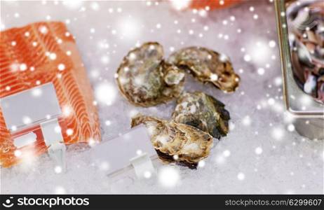 seafood, sale and food concept - chilled fresh fish and oysters on ice at grocery stall over snow. salmon fish and oysters on ice at grocery stall