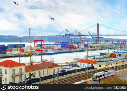 Seagulls over Lisbon commercial port, ships containers and freight cranes, skyline with 25th April Bridge and Tagus river, Portugal