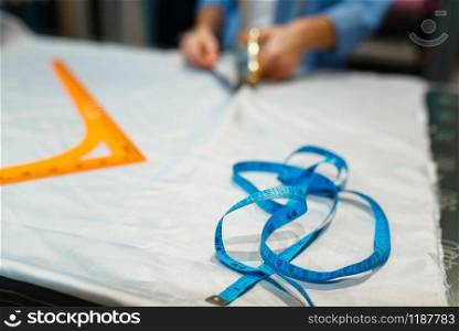 Seamstress cuts fabric with scissors in textile workshop. Woman works with cloth for sewing, female tailor at workplace. Seamstress cuts fabric with scissors in workshop