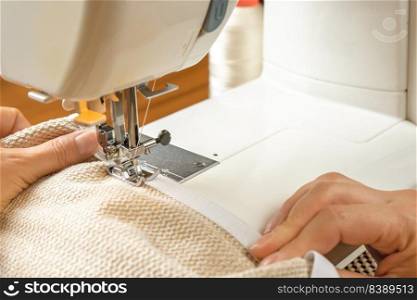 Seamstress hands holding white textile fabric. Female hands stitching white fabric on modern sewing machine at workplace. Close up view of sewing process. Handmade, hobby, small business concept. Female hands stitching white fabric on modern sewing machine. Close up view of sewing process.
