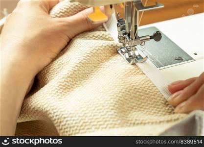 Seamstress hands holding white textile fabric. Female hands stitching white fabric on modern sewing machine at workplace. Close up view of sewing process. Handmade, hobby, small business concept. Female hands stitching white fabric on modern sewing machine. Close up view of sewing process.