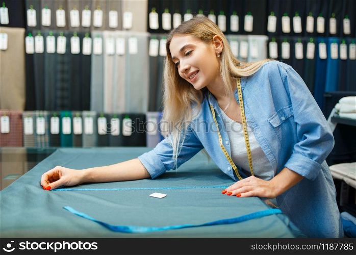 Seamstress measures fabric material in textile workshop. Woman works with cloth for sewing, female tailor at workplace, dressmaker. Seamstress measures fabric material in workshop