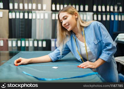 Seamstress measures fabric material in textile workshop. Woman works with cloth for sewing, female tailor at workplace, dressmaker. Seamstress measures fabric material in workshop