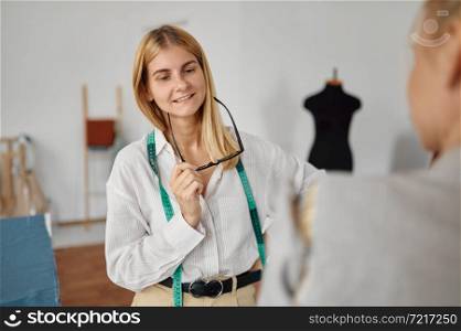 Seamstress takes measurements from woman in workshop. Dressmaking occupation and professional sewing, handmade tailoring business, handicraft hobby. Seamstress takes measurements from woman, workshop