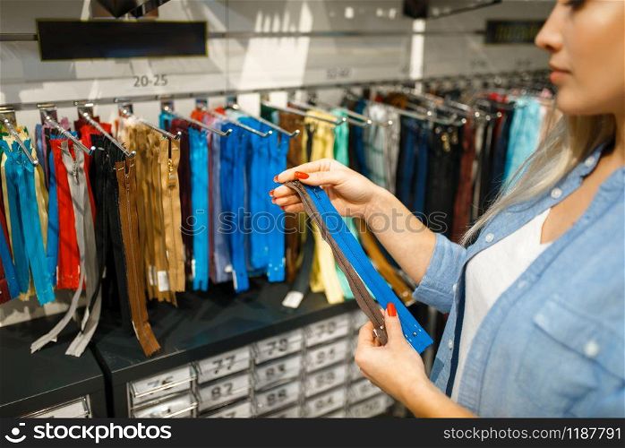 Seamstress takes zipper in textile workshop. Woman choosing cloth for sewing, female tailor at workplace, dressmaker. Seamstress takes zipper in textile workshop