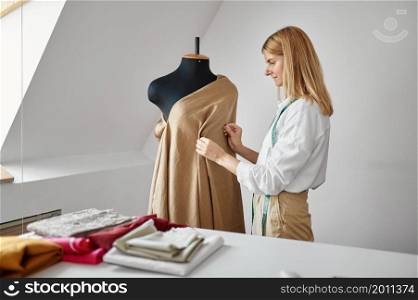Seamstress tries on a dress on a mannequin at her workplace in workshop. Dressmaking occupation and professional sewing, handmade tailoring business. Seamstress tries on dress on mannequin in workshop