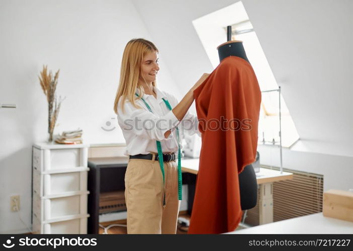 Seamstress tries on a dress on a mannequin at her workplace in workshop. Dressmaking occupation and professional sewing, handmade tailoring business, handicraft hobby. Seamstress tries on dress on mannequin in workshop