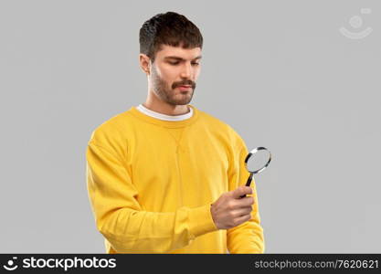 search, education and people concept - young man in yellow sweatshirt with magnifier over grey background. man in yellow sweatshirt with magnifier