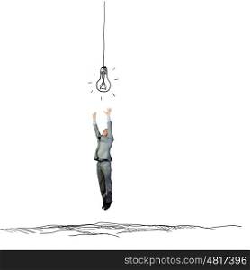 Search for inspiration. Young businessman jumping to catch drawn bulb. Idea concept