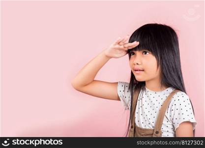 Searching concept. Asian little kid 10 years old looking far away with hand over head at studio shot isolated on pink background, Portrait of Happy child girl looking at distance with eyes shaded
