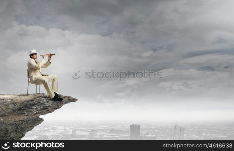 Searching for future perspectives. Businessman in white suit and hat sitting in chair and looking in spyglass