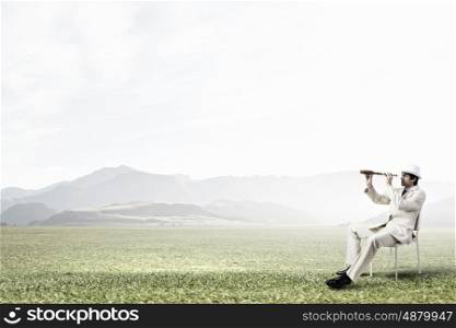 Searching for future perspectives. Businessman in white suit and hat sitting in chair and looking in spyglass