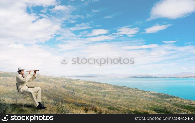 Searching for future perspectives. Businessman in white suit and hat sitting in chair and looking in spyglass