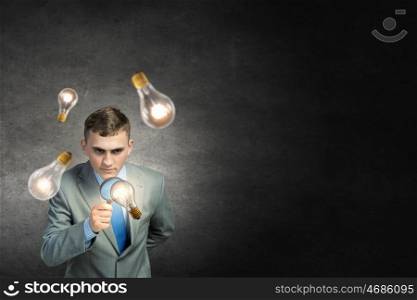 Searching for idea. Young businessman looking in magnifying glass at glass light bulb