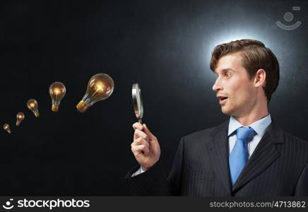 Searching for idea. Young businessman looking in magnifying glass at glass light bulb