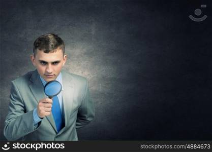 Searching for idea. Young businessman looking in magnifying glass at glass light bulb
