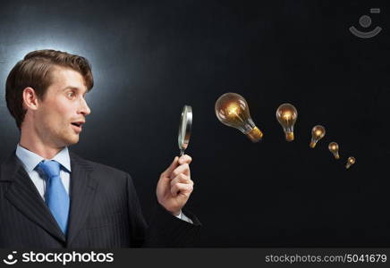 Searching for idea. Young businessman looking in magnifying glass at glass light bulb